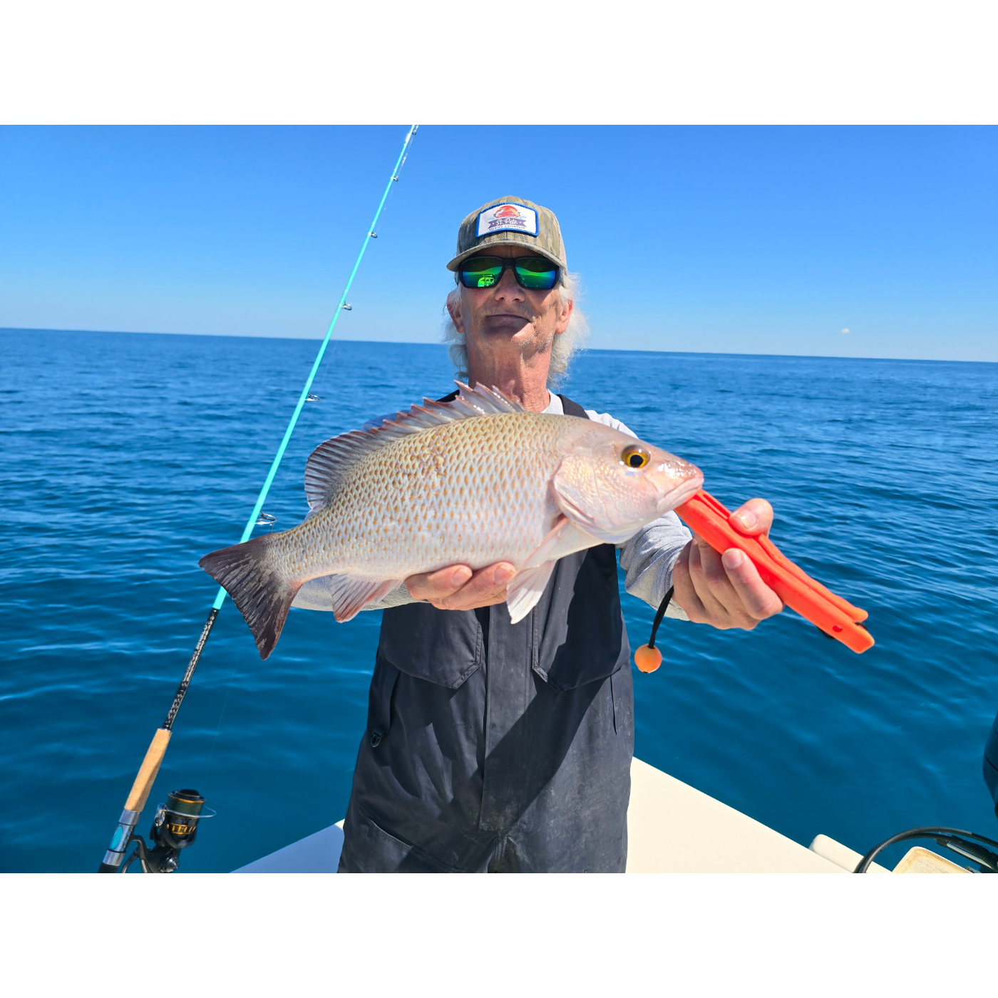 Man holding a fish and fishing equipment on a boat with blue water and sky in the background