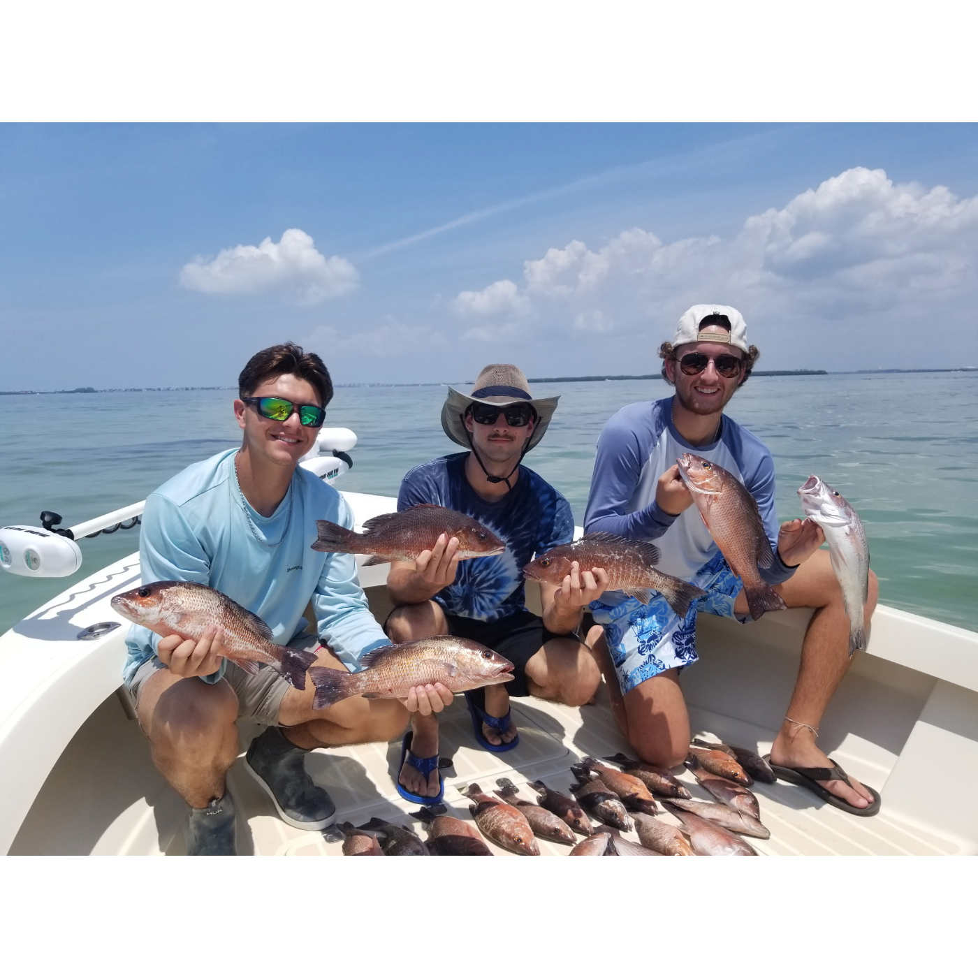 Three men on a boat holding fish with a clear sky and water background