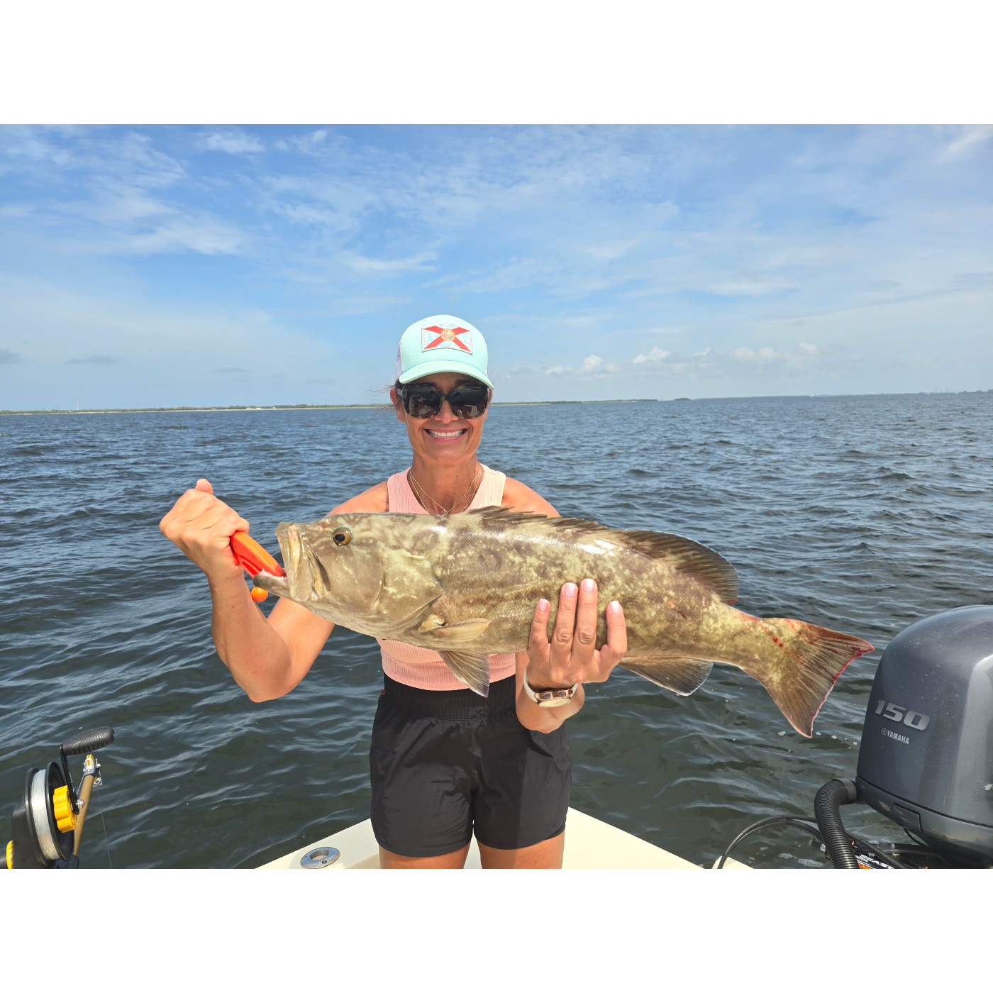 Person holding a large fish on a boat with a clear sky and water background