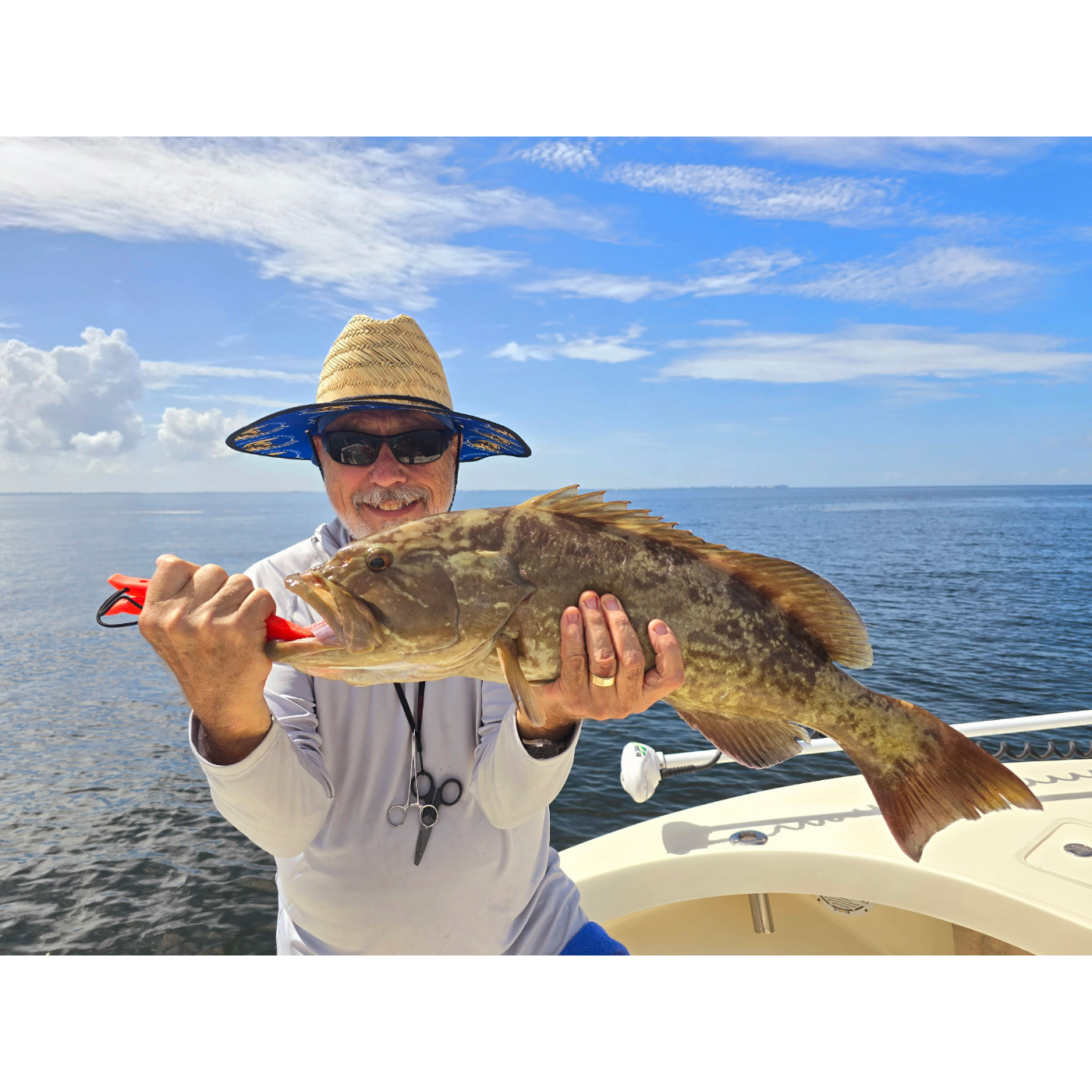 Man holding a large fish on a boat with a clear blue sky and ocean background