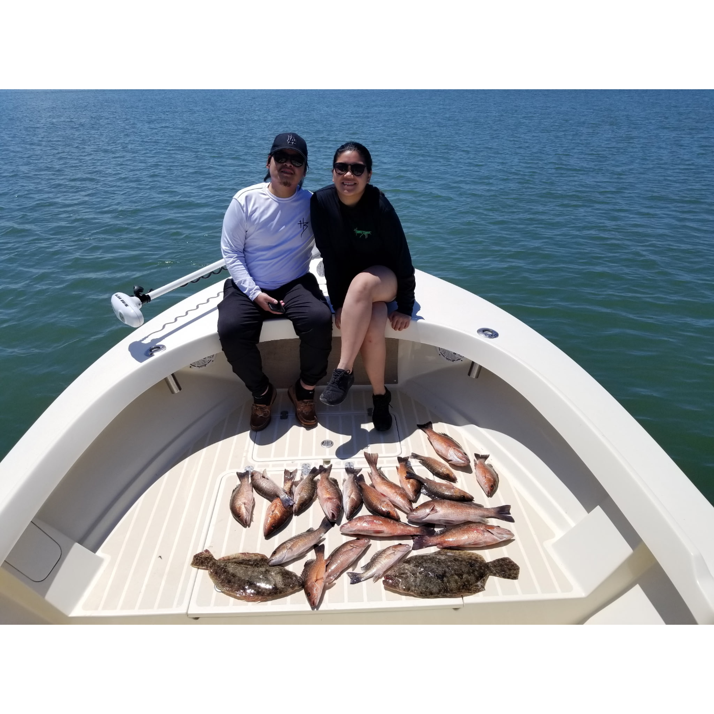 Two people on a boat with a catch of fish on a clear day.