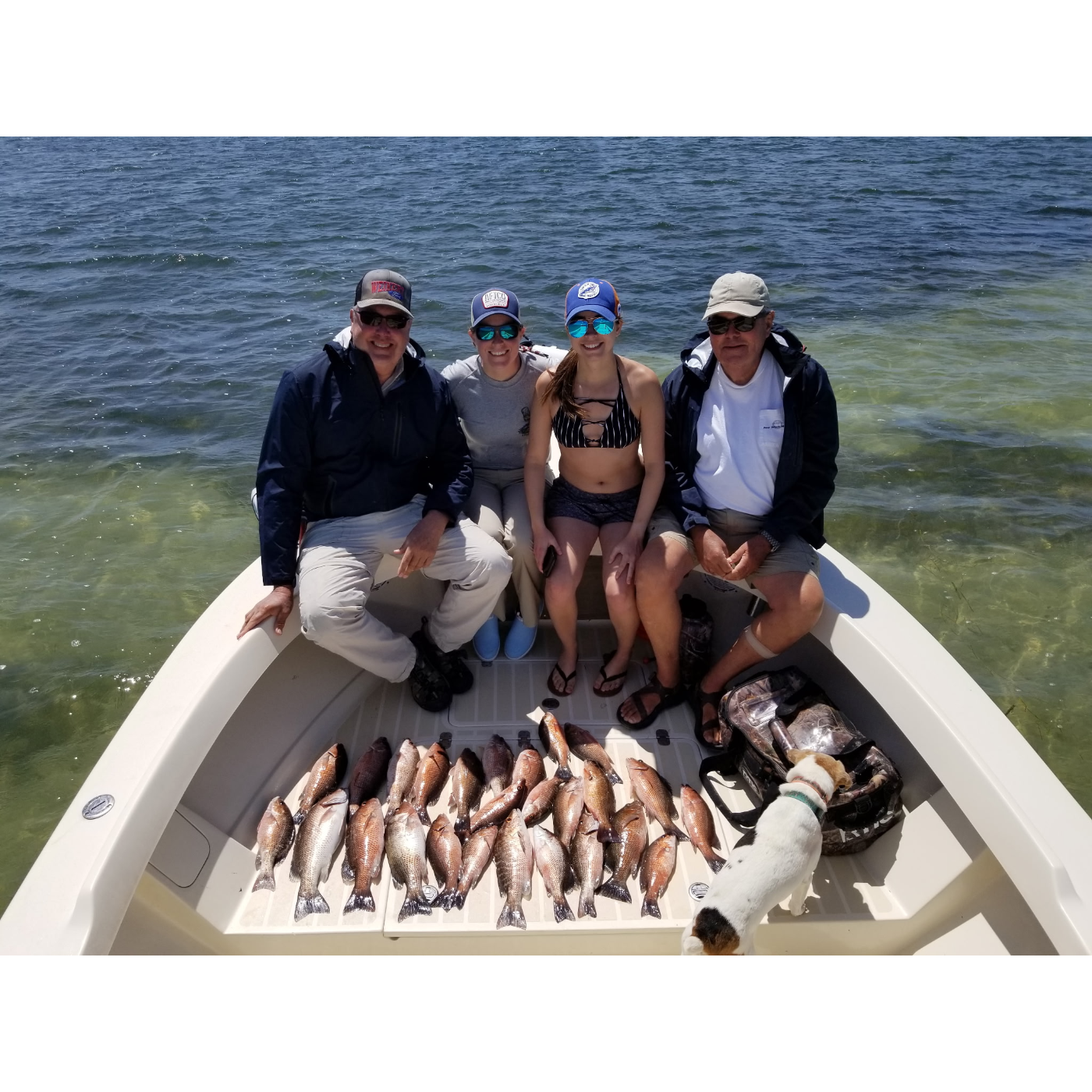 Four people on a boat with a catch of fish in a body of water.