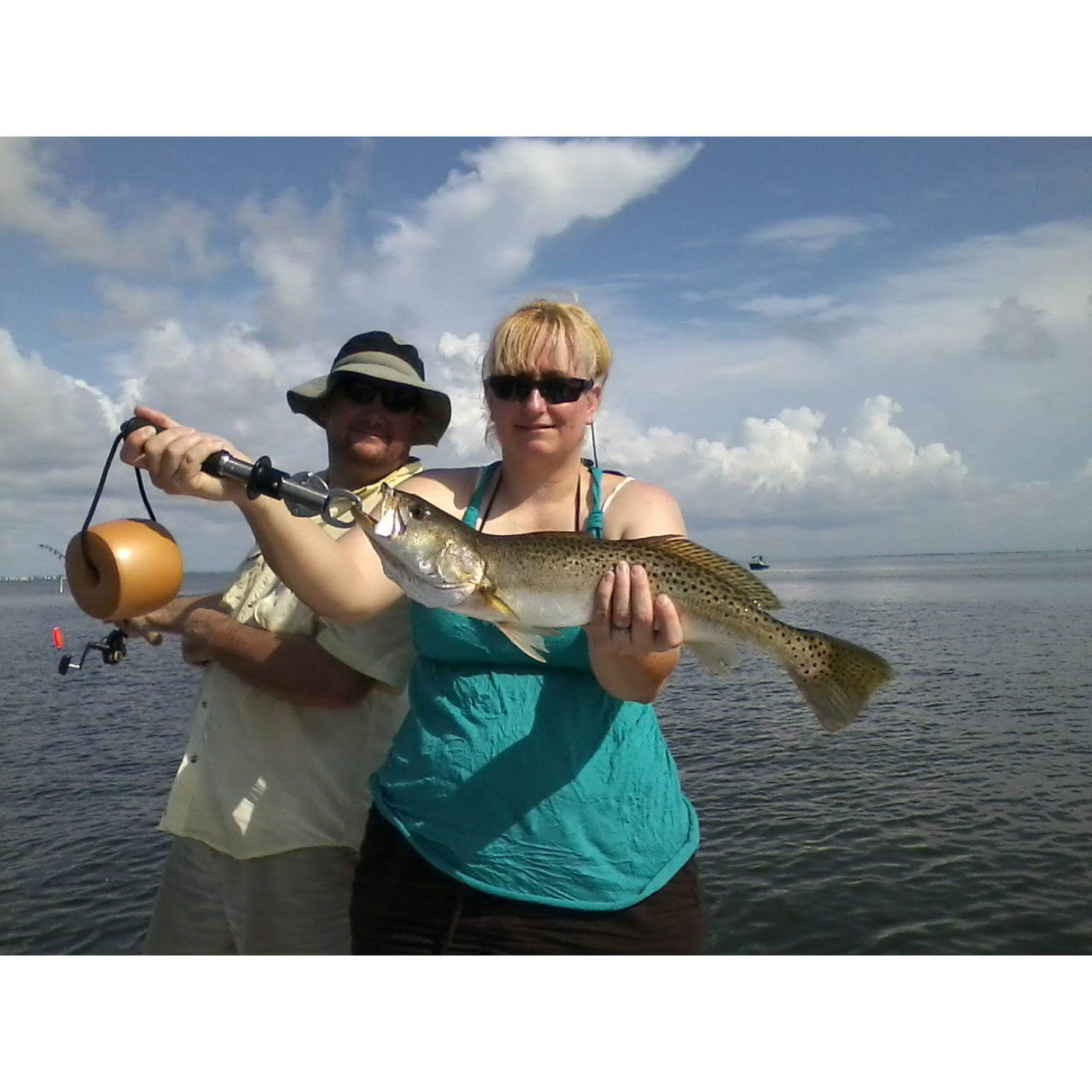 Two people holding a fish on a body of water with a cloudy sky.