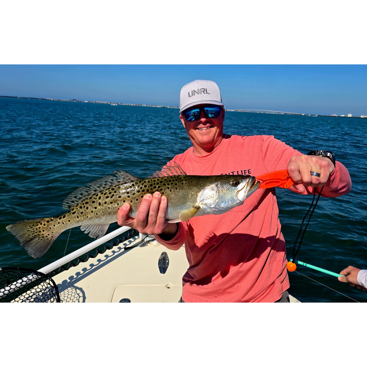 Man holding a fish on a boat with a clear blue sky and water background
