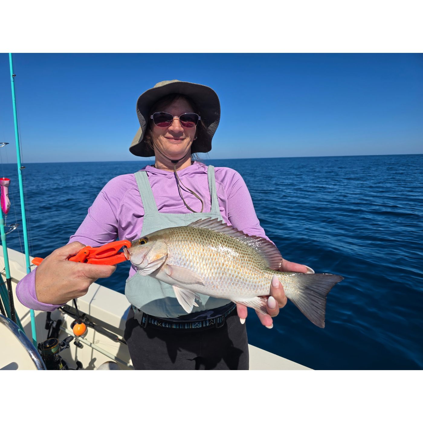 Person holding a fish on a boat with a clear blue sky and water background