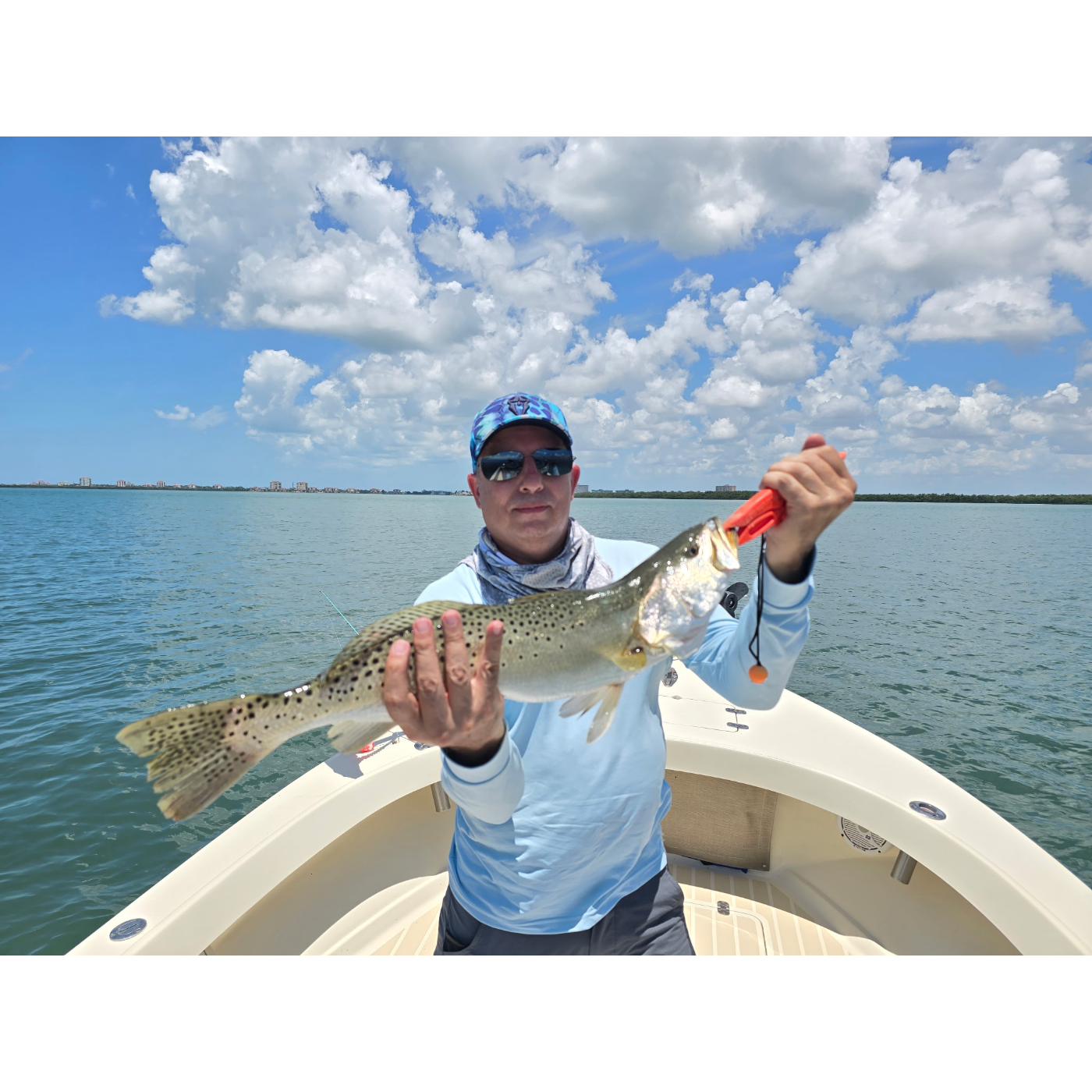 Man holding a fish on a boat with a blue sky and clouds in the background